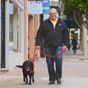 Man walking black dog on city sidewalk.